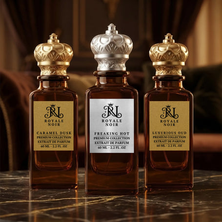 Royale Noir unisex fragrance collection with elegant amber glass bottles, gold labels, and crown-shaped caps in a luxury setting